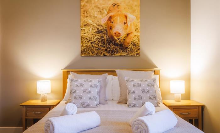 Large pig wall canvas above double bed and side tables with lamps and pig themed cushions and white fluffy towels.